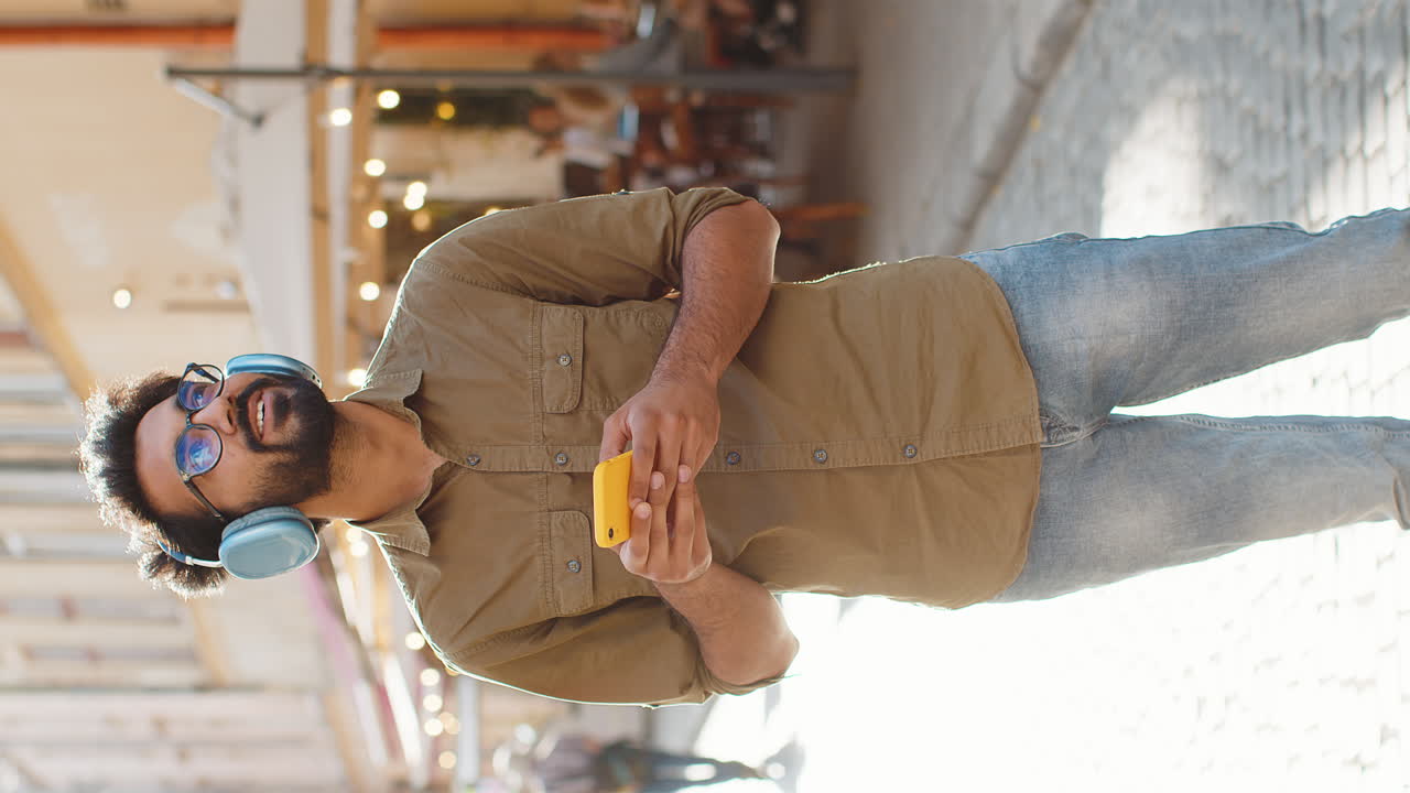Happy young man in wireless headphones choosing listening music in smartphone dancing outdoors