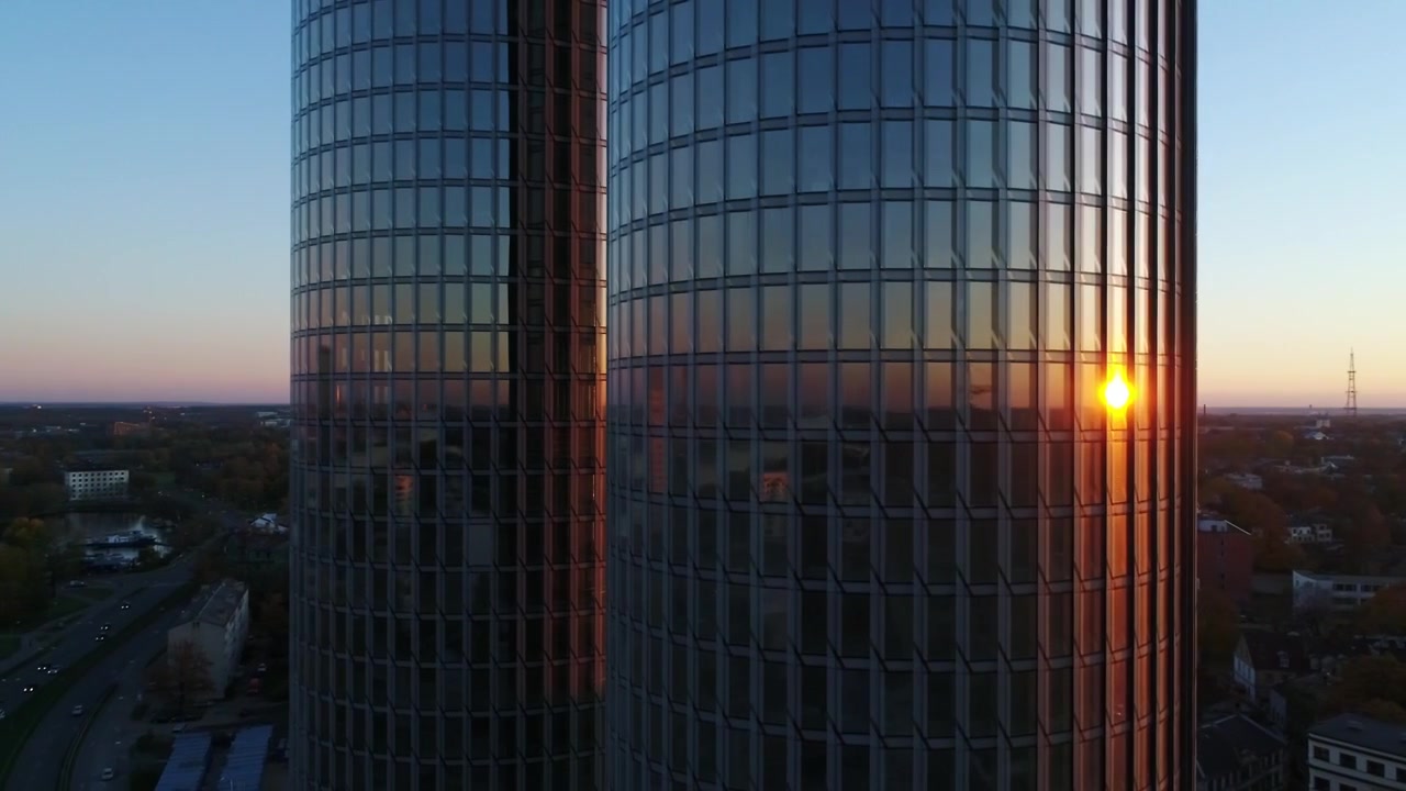 Drone orbitando, torres gêmeas de Riga refletindo o pôr do sol quente nas paredes de vidro.