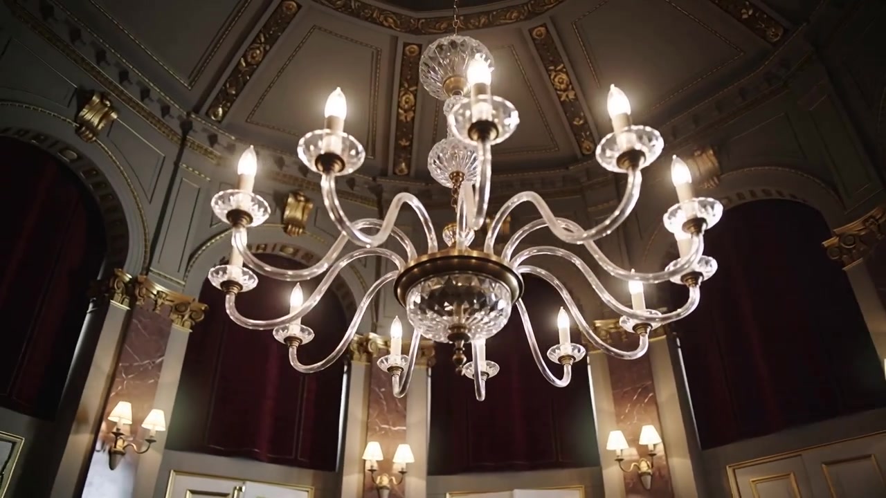 La telecamera panoramica attorno a un lampadario a più bracci mostrando un soffitto dorato e drappeggi rossi per mostrare i dettagli.