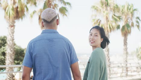 Portrait-of-happy-biracial-couple-holding-hands-on-promenade,-in-slow-motion