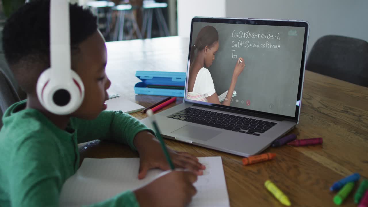 African american boy doing homework while having a video call with female teacher on laptop at home
