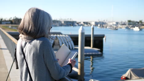 a middle aged woman author with writers block looking at the pages of a blank book as she thinks about writing at the ocean