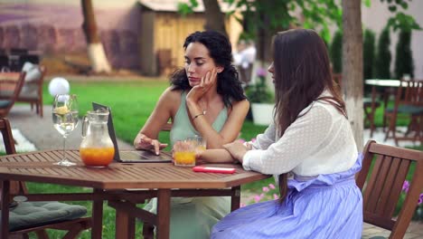 Two-women-sitting-at-the-outdoors-cafe---talking,-sharing-news,-brunette-girl-listen-carefully