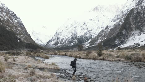 Girl-walking-along-river-surrounded-by-valleys-and-snow-capped-mountains-in-New-Zealand