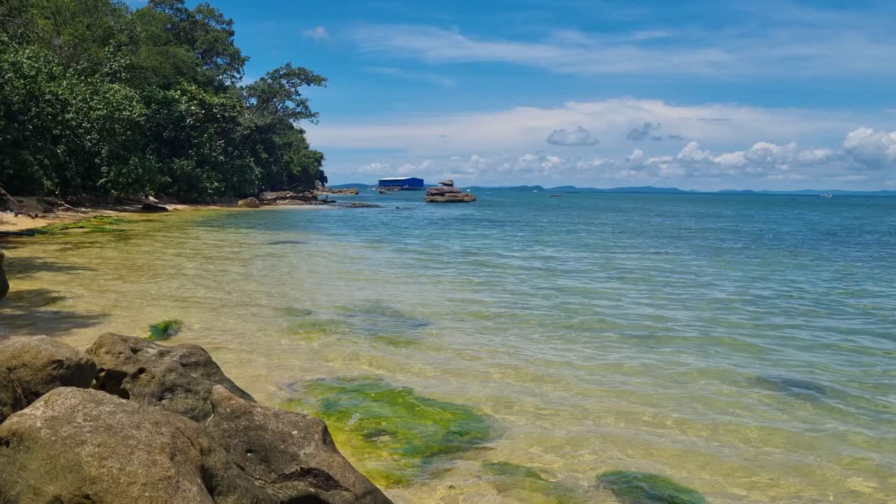 Picturesque tropical beach on Phu Quoc, Vietnam, near Starfish Beach, with turquoise waves gently lapping the rocky shore under a clear blue sky, framed by lush coastal scenery