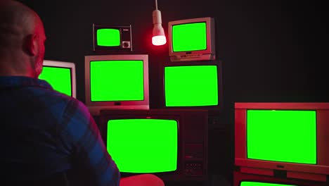 an elderly man is sitting in front of old televisions