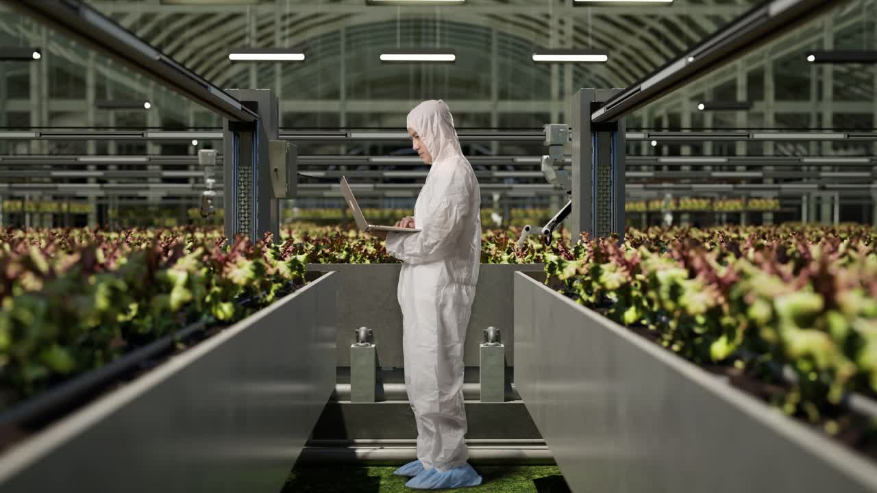 полный вид тела азиатского исследователя, использующего ноутбук, стоя в теплице с умными роботами-фермерами