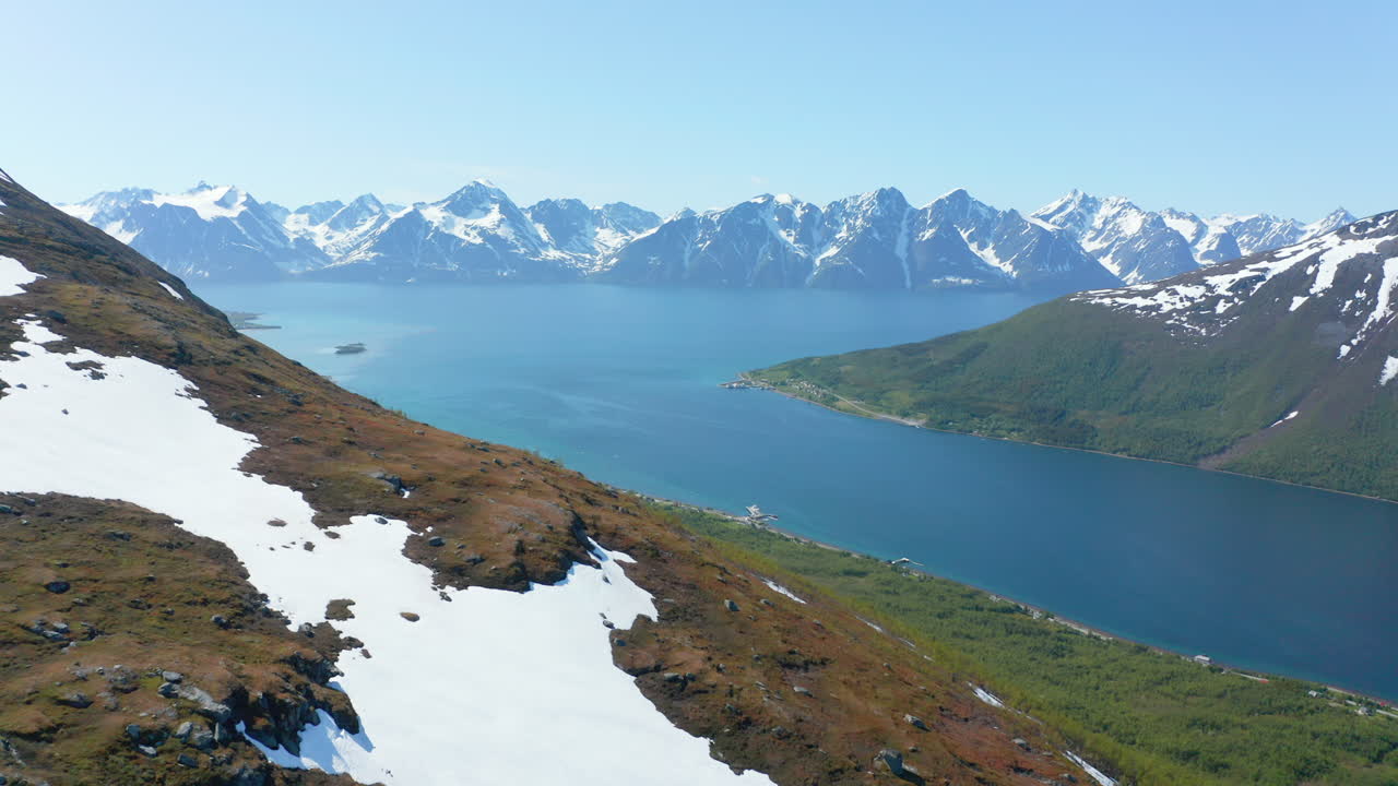 vista aérea sobre una montaña nevada, hacia el mar de barents y los alpes de lyngen, soleado, día de verano, en rotsund, troms, nordland, noruega - dolly, drone shot