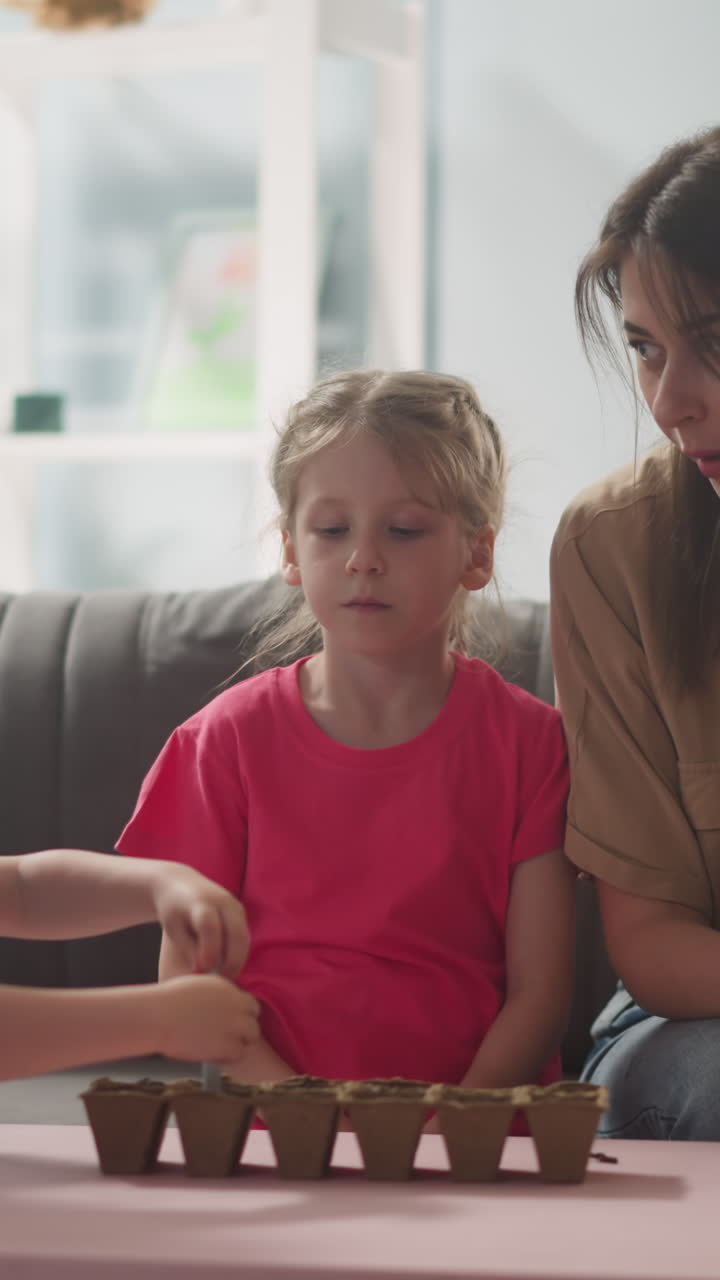 woman teaches children how to plant flowers, little child makes holes in ground to plant seeds in pots, indoor plants, mother with son and daughter spend time together