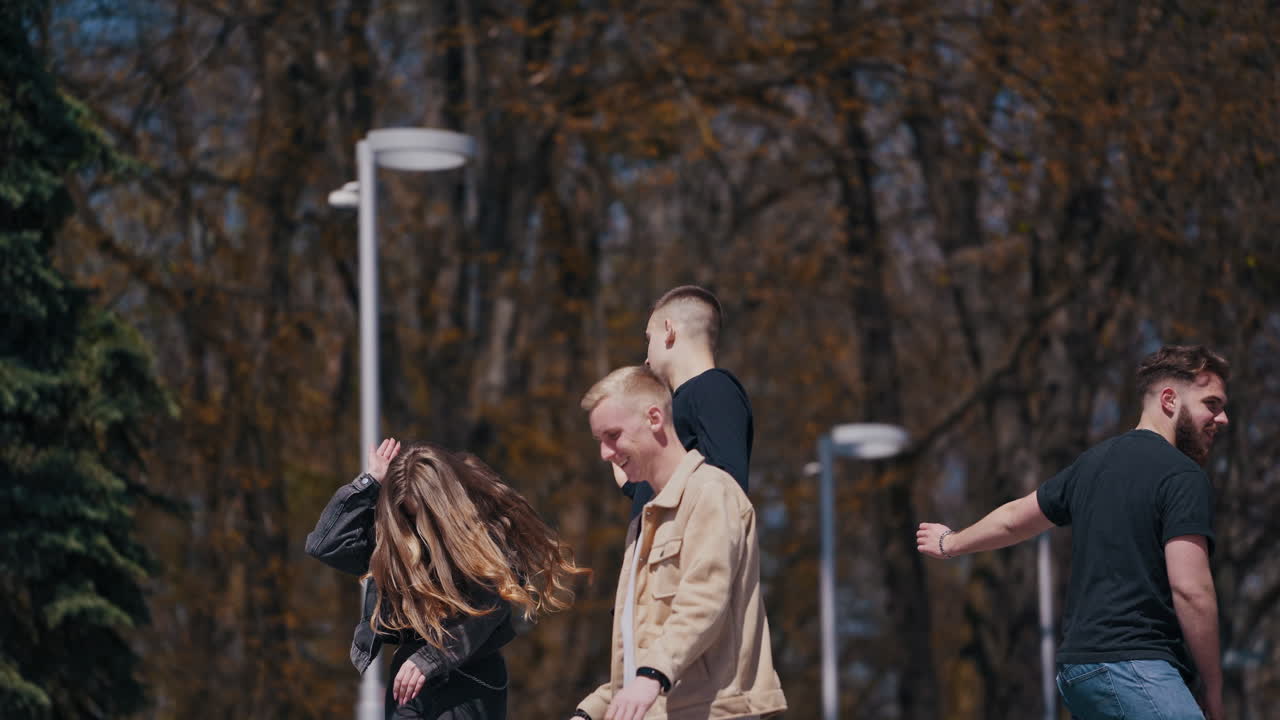 Funny young people dancing and jumping outdoors. Group of guys and a girl having joy together in the city park in sunny autumn day. Happy friendship concept