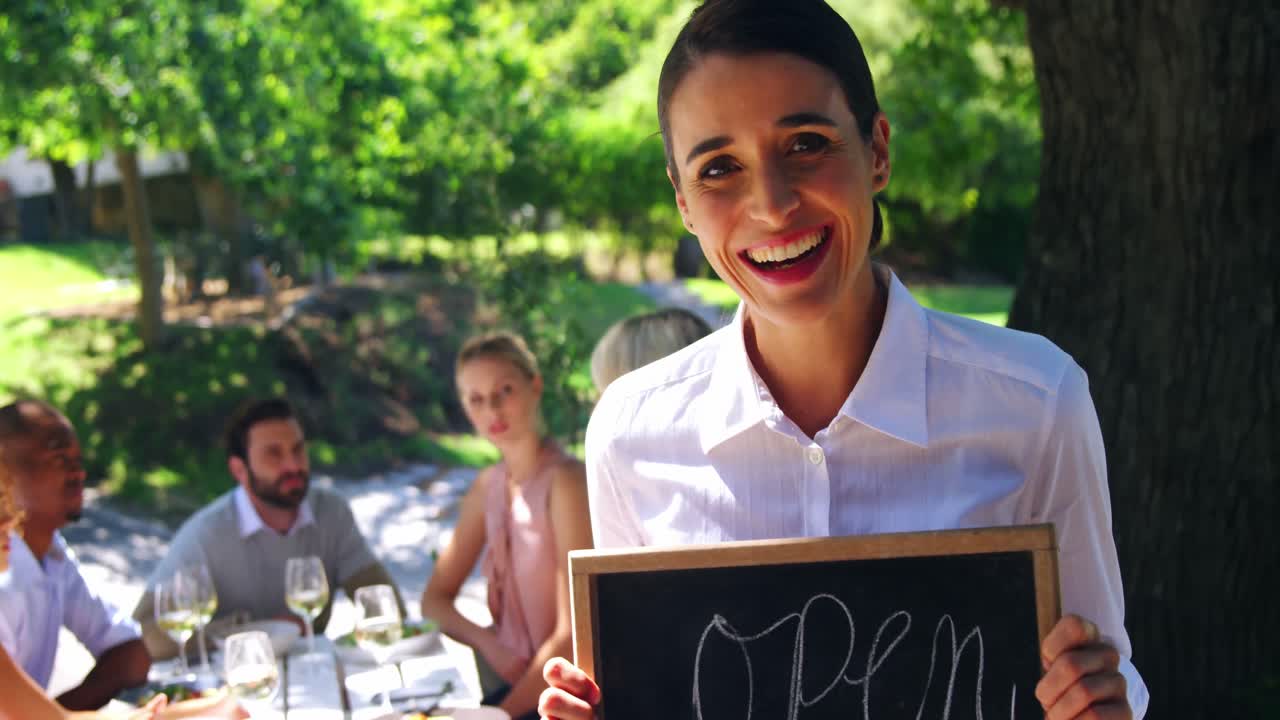 camarera sonriente mostrando la pizarra con un letrero abierto
