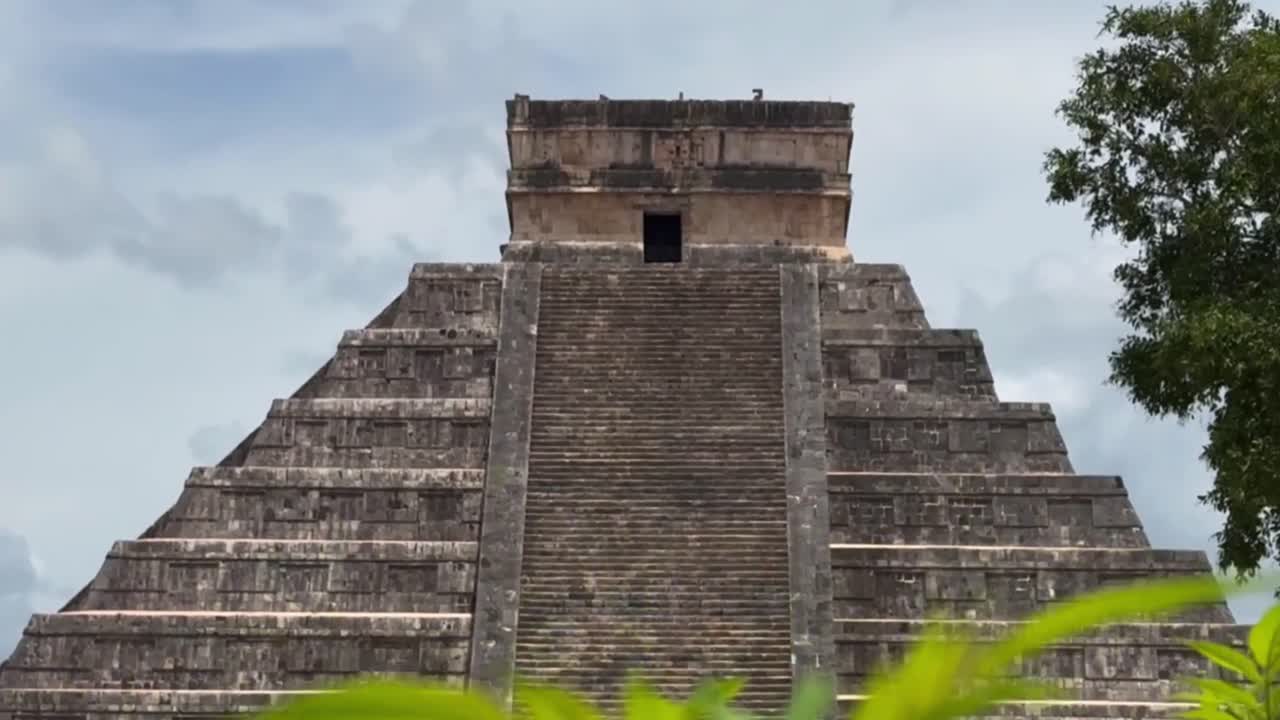 Handheld booming up long lens shot from plants to El Castillo ancient Mayan pyramid in Chichen Itza, Mexico. 4K