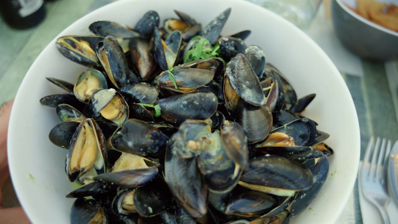 Mejillones recién cocinados servidos en un cuenco blanco con una salsa cremosa y hierbas verdes, ofreciendo un delicioso plato de marisco