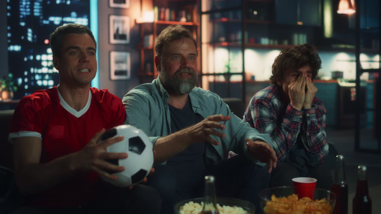 noche en casa: tres alegres aficionados al fútbol sentados en un sofá viendo el juego en la televisión, celebrando la victoria cuando el equipo deportivo gana el campeonato. grupo de amigos aplauden el juego del club de fútbol favorito. cámara lenta