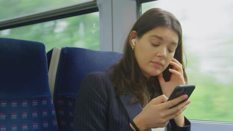 businesswoman with wireless earbuds commuting to work on train looking at mobile phone