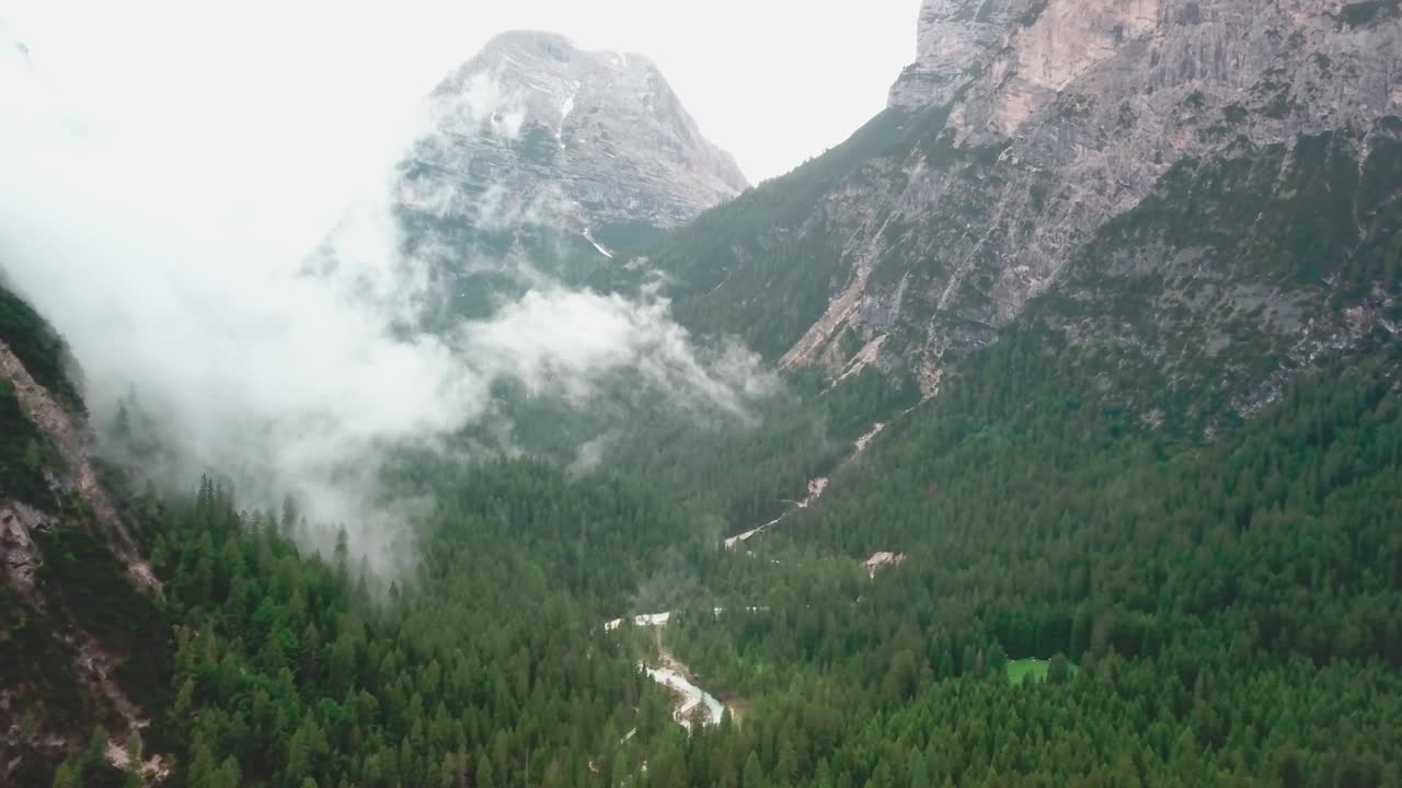 Dolly, tilt down drone shot of the Alps with low clouds and rocky cliffs