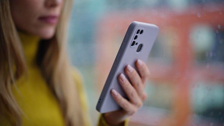Donna in carriera che scorre un messaggio sul telefono mentre è in piedi vicino alla finestra, primo piano