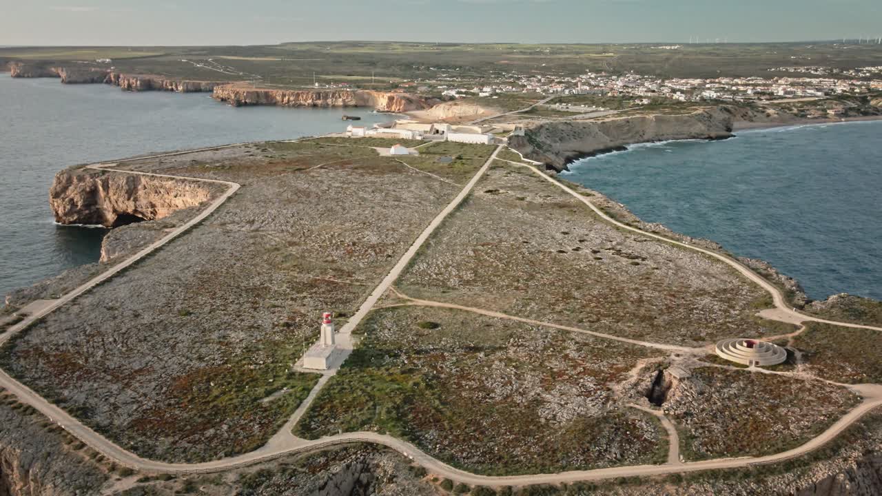 Cinematic aerial shot drifting backward to unveil the dramatic cliffs, fort, and lighthouse at Sagres—the southwestern tip of Portugal, surrounded by ocean