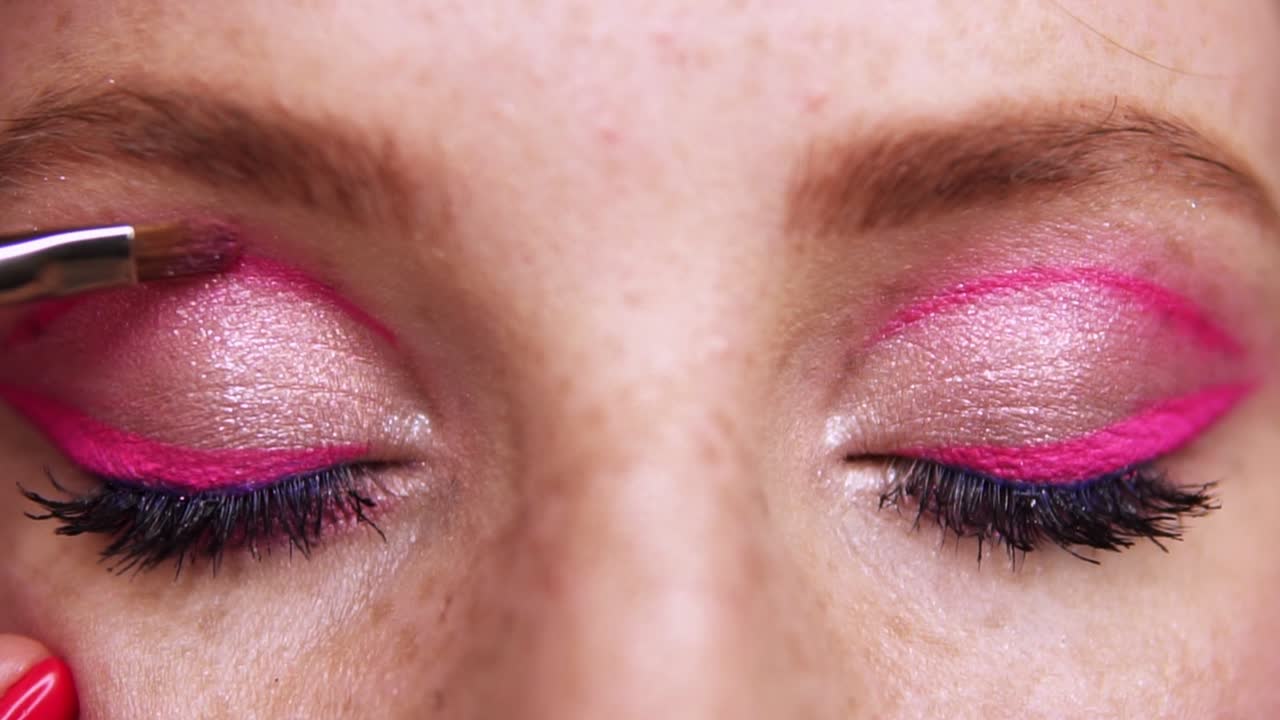 primer plano de los ojos de una mujer joven durante el maquillaje profesional. el artista de maquillaje aplica sombras rosadas en el ojo de la chica con un pincel. moda y belleza