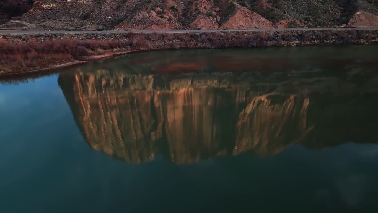 Aerial Moab canyon establishing at sunset, reflection of long shadows over towering red rock cliffs and deep valleys in water shimmering