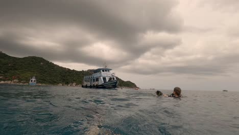 a blonde girl is swimming back to her boat