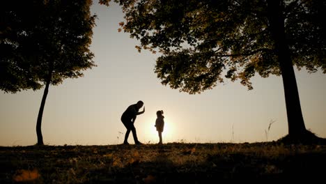 against the background of the bright orange sunset sky, the silhouette of the father hugs his daughter, circles her and throws her up