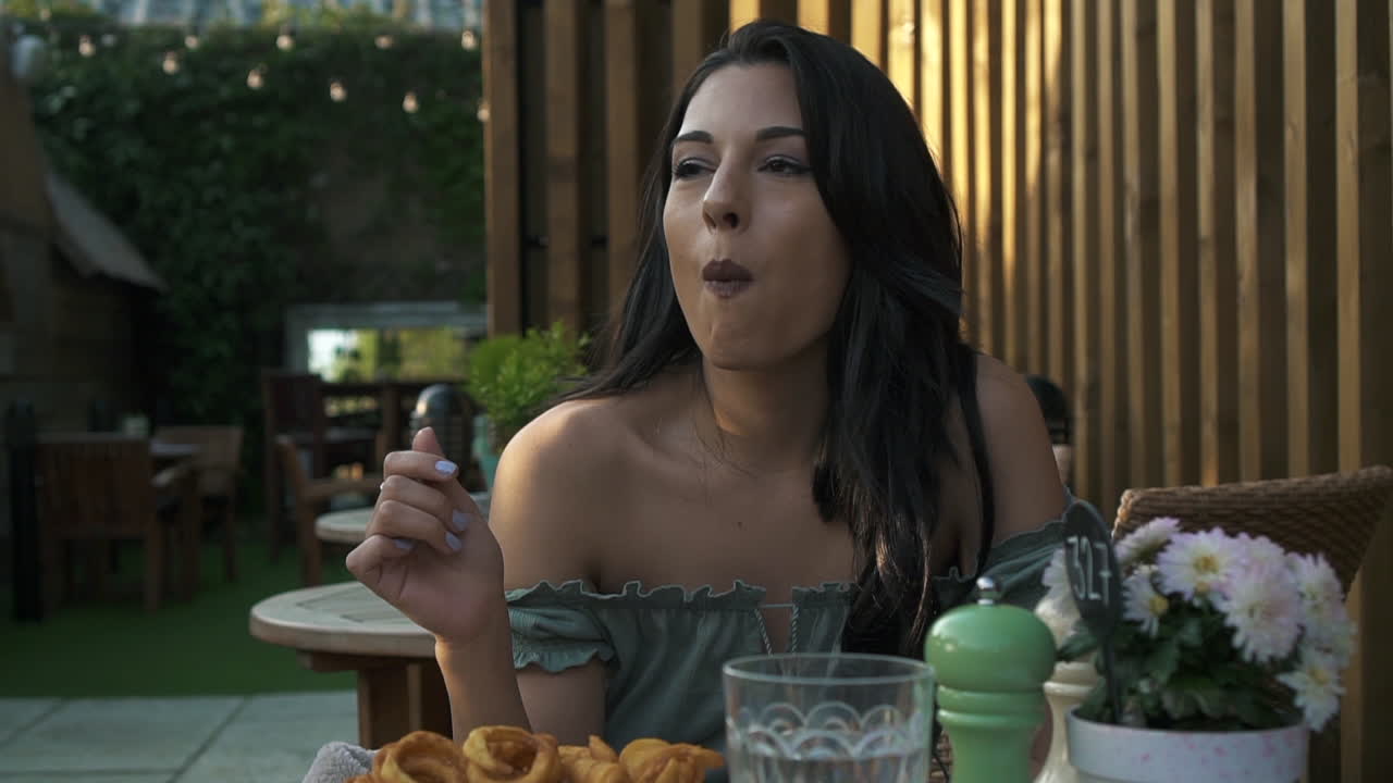 adorable mujer comiendo papas fritas rizadas en un café en londres, latina hispana milenaria en la mesa vestida informal, comiendo y divirtiéndose, sonriendo y disfrutando de la comida rápida