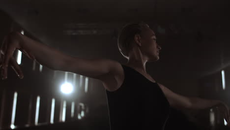 Close-up-of-ballet-dancer-as-she-practices-exercises-on-dark-stage-or-studio.-Ballerina-shows-classic-ballet-pas.-Slow-motion.-Flare-gimbal-shot.