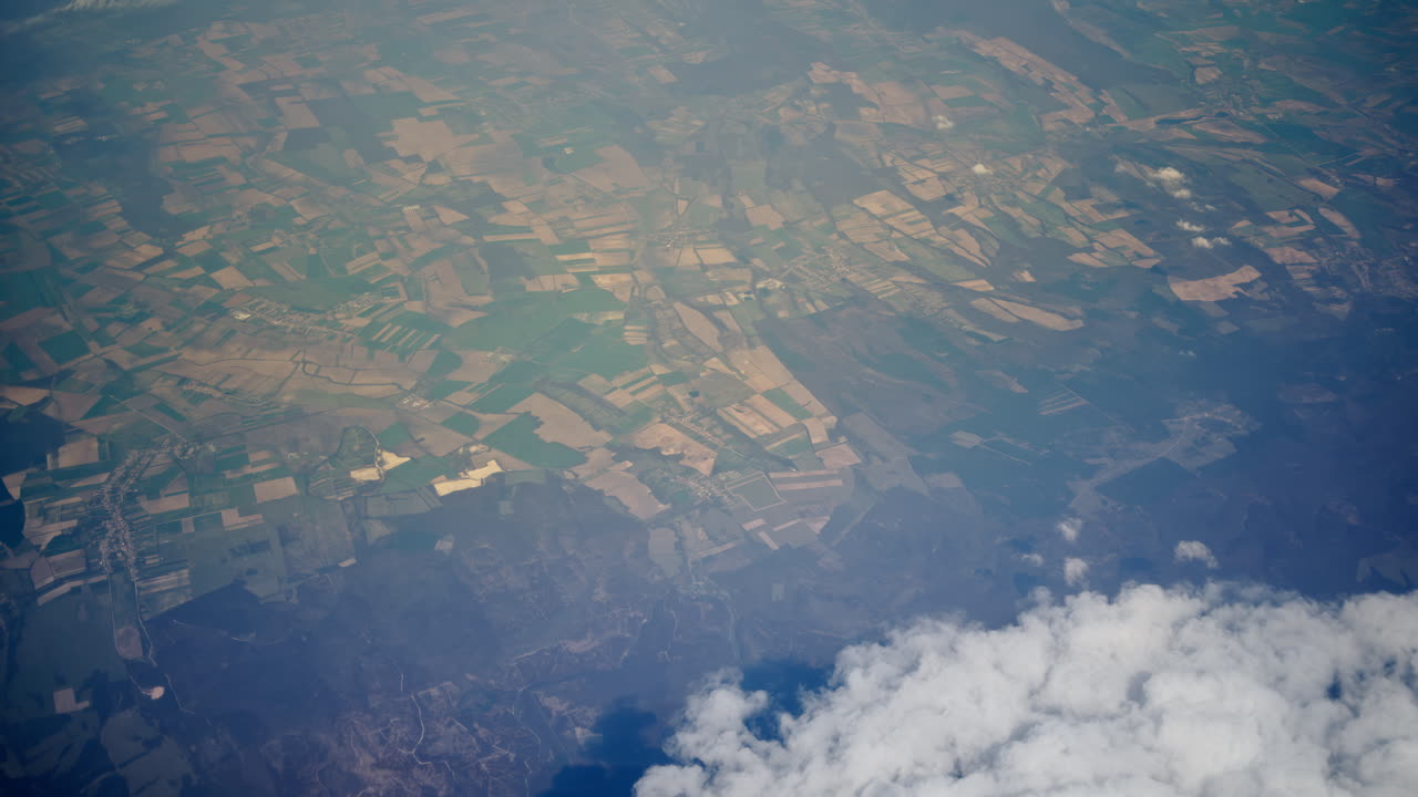 Aerial view of white, fluffy clouds above fields seen from an airplane window