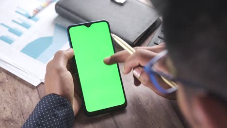 person using smartphone with green screen at a desk