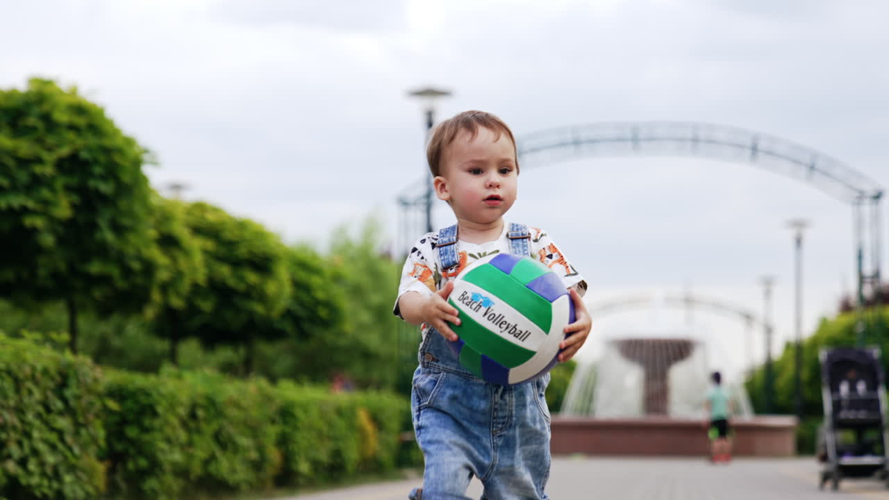 Happy Caucasian baby boy runs with a ball smiling cheerfully. Kid runs up to camera and throws the ball. Low angle view.