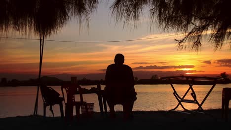 Silueta-De-Un-Hombre-Sentado-En-La-Orilla-Del-Río-Y-Disfrutando-Del-Atardecer-De-Verano-En-Kampot,-Camboya