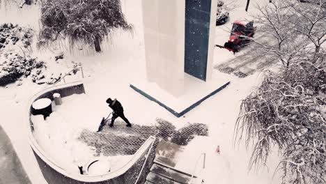 man with shovel cleaning the road from snow in an urban context