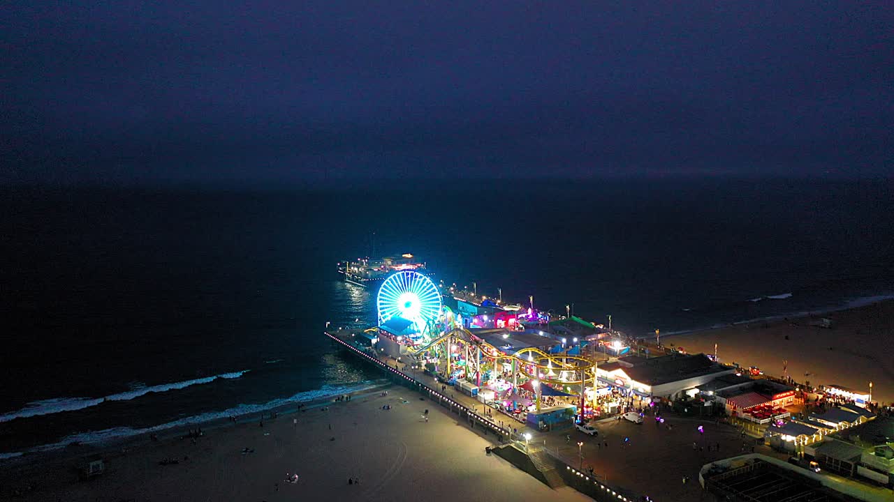 Santa Monica Pier at night aerial drone rotating view of the roller coaster and ferris wheel