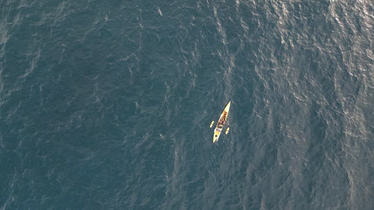 vista aérea de arriba hacia abajo de un kayak de pesca individual amarillo flotando en el océano con el reflejo del sol de la mañana