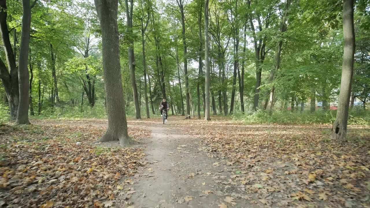 Front view of man on bicycle with glasses riding away in the forest road. Man on a mountain bike rides through the forest in summer sunrise.