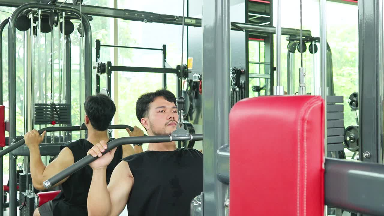 Two men perform pull-down exercises in a gym, focusing on strength and muscle building in a bright, modern environment