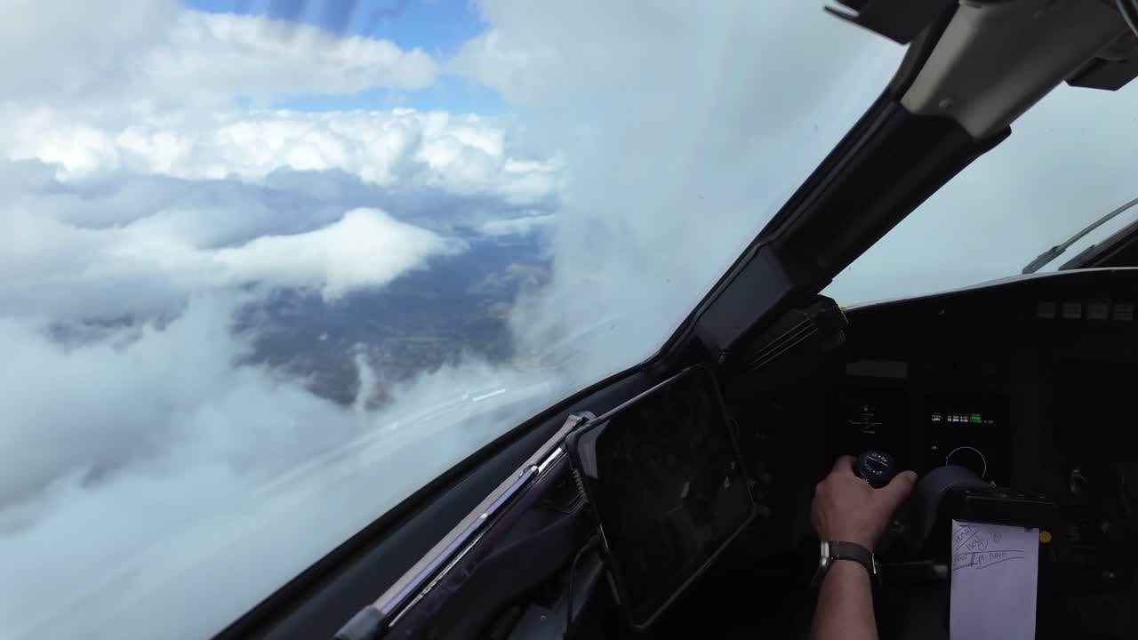 A pilot perspective from inside a jet airplane cockpit, flying manually while exiting from storm clouds into clear skies. Captain is piloting.