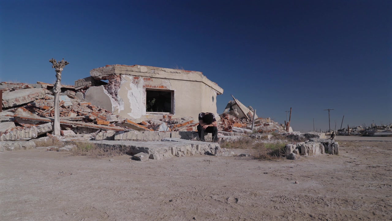 Uomo seduto tra le rovine coperte di sale di Villa Epecuen ad Adolfo Alsina, Provincia di Buenos Aires, Argentina, abbandonata dopo l'alluvione catastrofica del Lago Epecuen, inquadratura statica
