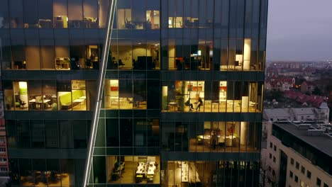 drone shot at a night skyscraper with office windows and business people working late at computers.