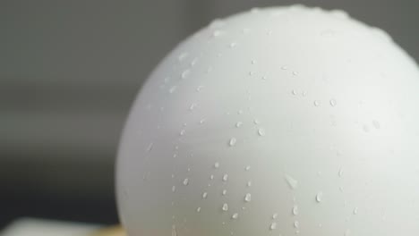 close up of a white plain sphere wet spinning with reflecting water drops on the sphere. a dark gray background. shot in slow motion in 4k.