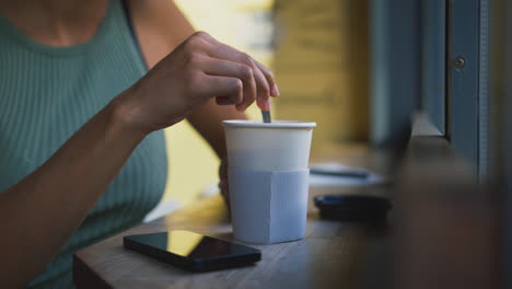 close up of female customer in coffee shop window stirring hot drink