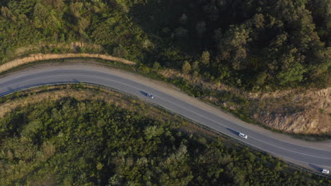 Cars-moving-on-a-mountain-road-with-green-forest-on-the-sides,-on-the-sunset,-Russia,-Far-East