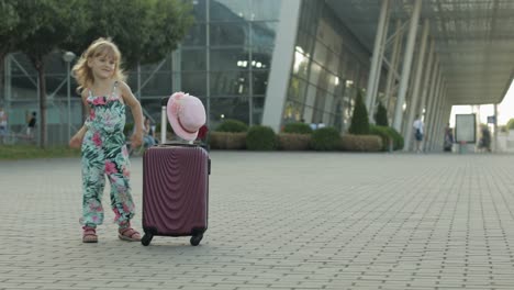 Child-girl-tourist-with-suitcase-bag-near-airport.-Kid-dances,-rejoices,-celebrates-with-luggage