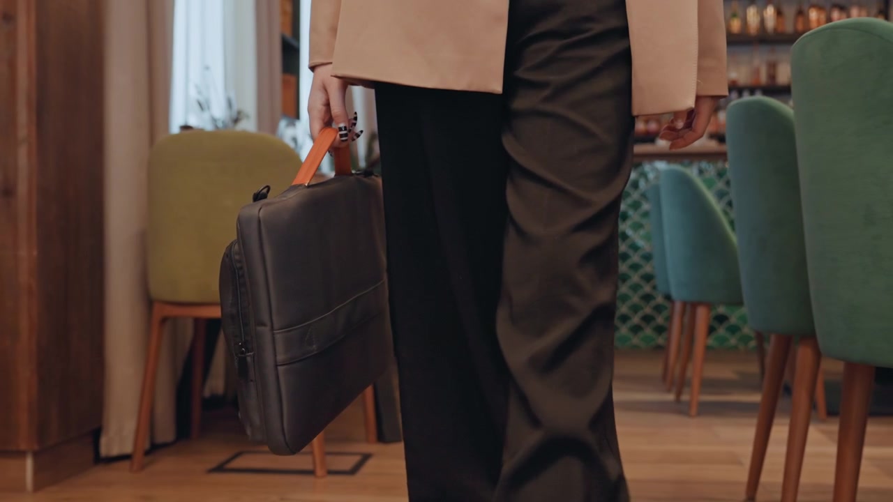 Imprenditore caucasico che esce da un caffè con una ventiquattrore, sedie verdi, sgabelli da bistrò, pavimento in legno, passo svelto, abbigliamento business casual, borsa in pelle che oscilla, illuminazione ambientale, energia da fine riunione