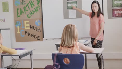 happy diverse female teacher and schoolgirls raising hands in elementary school class, slow motion