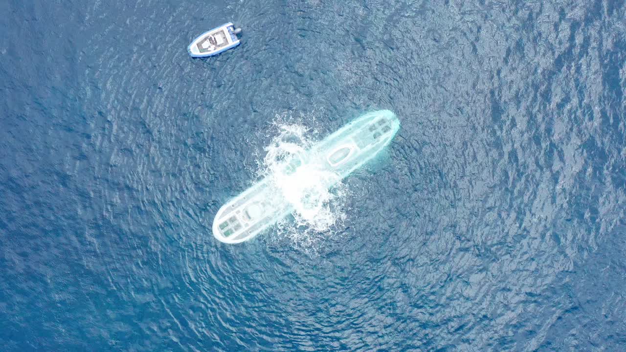 Aerial bird's eye close-up shot looking straight down at a submarine in the open ocean off the coast of Hawai'i as the ballast tank blows and the sub begins to dive underwater
