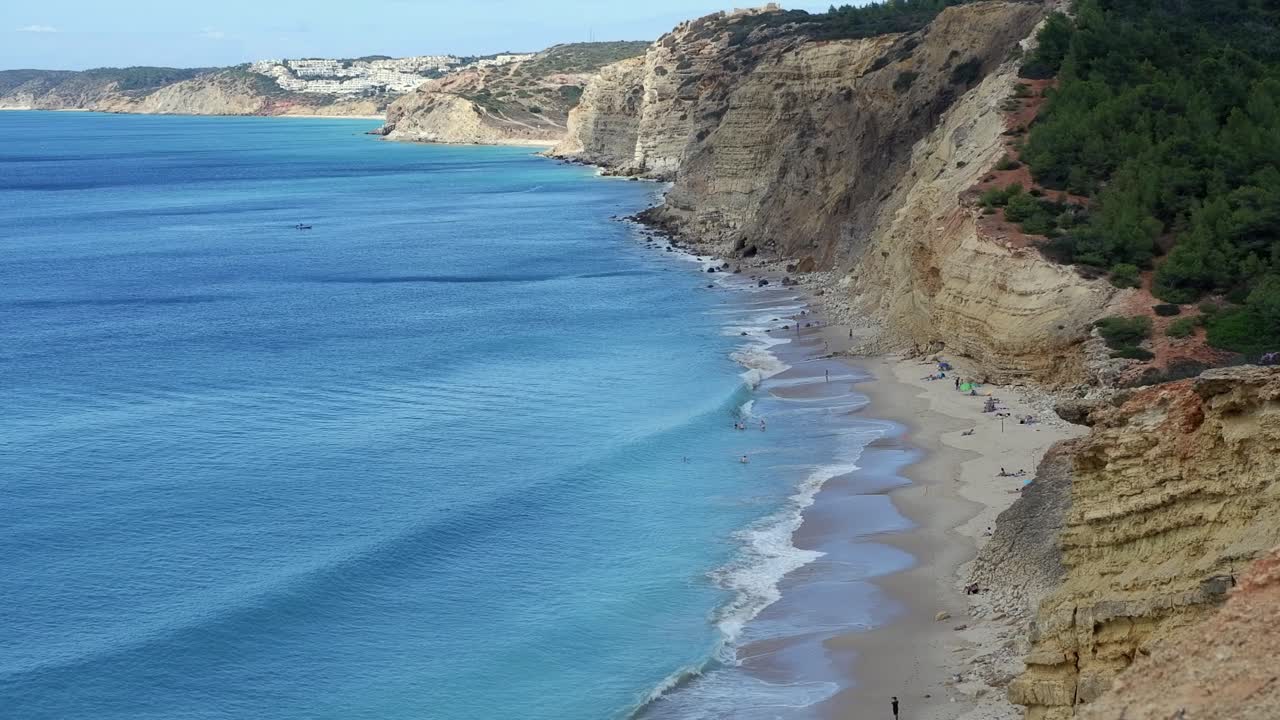 Few tourists enjoy sand ocean beach beneath rocky cliffs, calm water