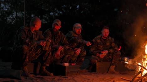 the military set up camp at night in the training areas, lit a campfire to warm up and frying sausages on sticks, the men were on duty, guarding the training ground, talking among themselves