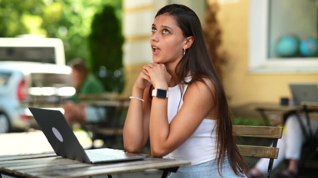 mujer joven trabajando en una computadora portátil en un café al aire libre